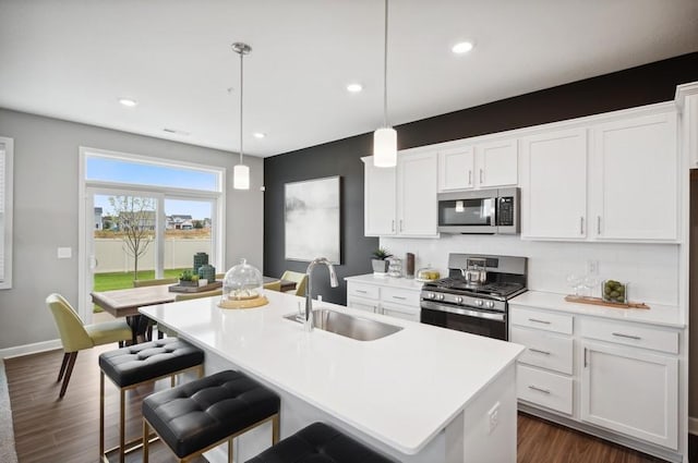 kitchen with a kitchen island with sink, sink, hanging light fixtures, and appliances with stainless steel finishes