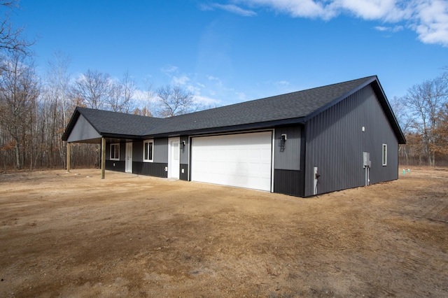 exterior space featuring an attached garage, a shingled roof, and dirt driveway