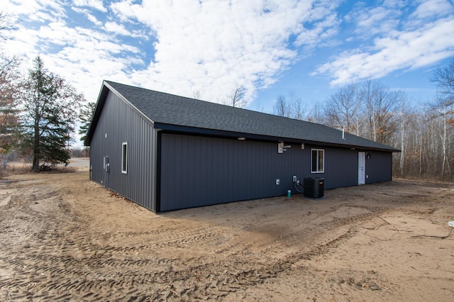 view of side of home featuring central AC unit and roof with shingles