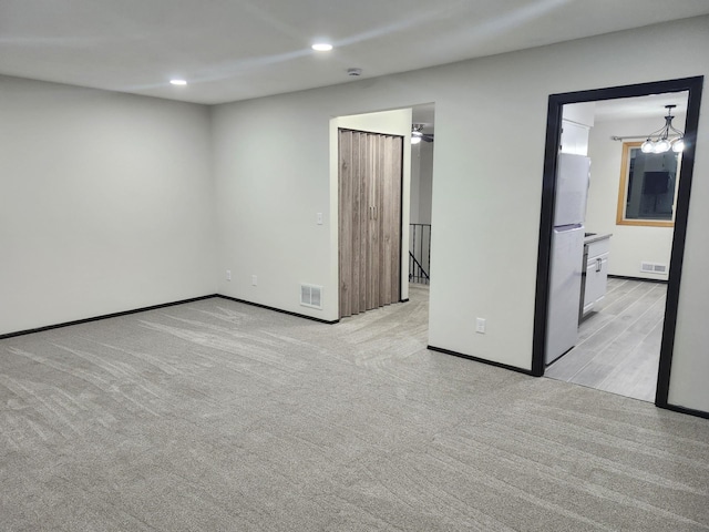 unfurnished bedroom featuring ensuite bathroom, an inviting chandelier, stainless steel fridge, and light carpet