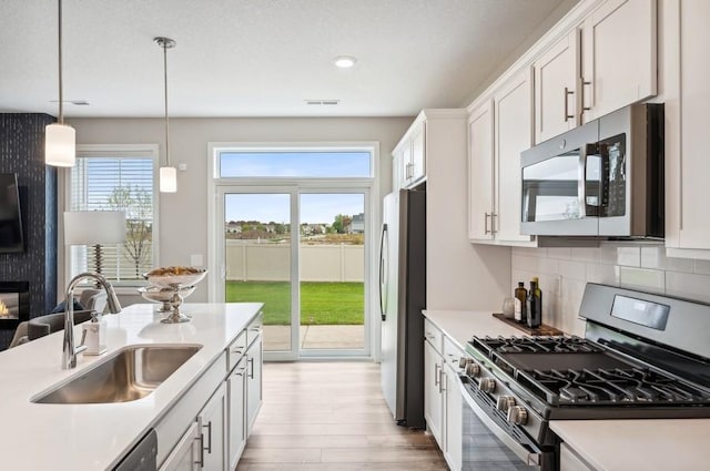 kitchen with pendant lighting, backsplash, white cabinets, sink, and stainless steel appliances