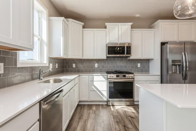 kitchen featuring backsplash, white cabinets, hanging light fixtures, light hardwood / wood-style flooring, and appliances with stainless steel finishes