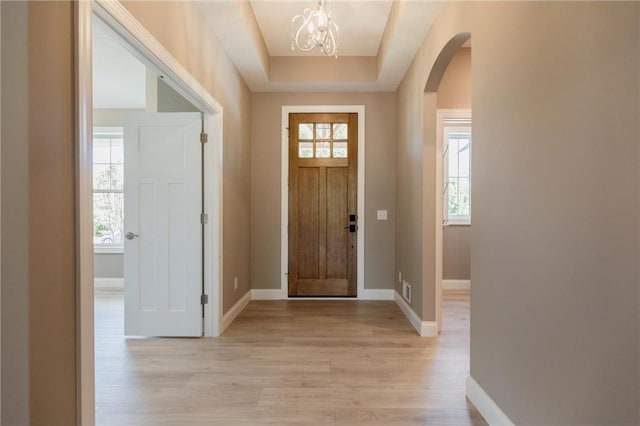 entrance foyer featuring arched walkways, a notable chandelier, baseboards, and light wood-style floors