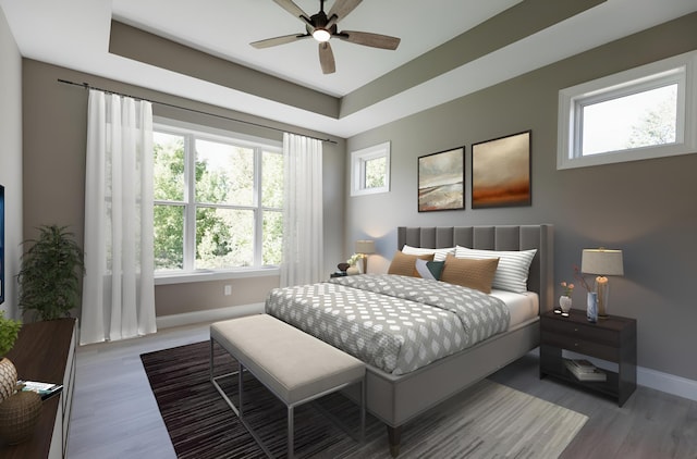 bedroom with ceiling fan, a tray ceiling, baseboards, and wood finished floors