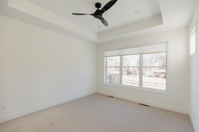 empty room featuring visible vents, ceiling fan, baseboards, a tray ceiling, and light carpet