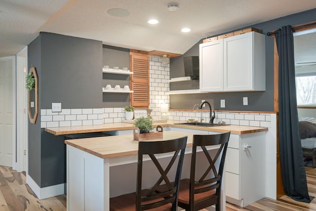 kitchen with sink, butcher block counters, white cabinets, a kitchen bar, and decorative backsplash