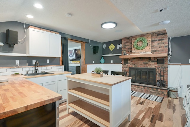 kitchen with butcher block counters, sink, white cabinetry, a brick fireplace, and light hardwood / wood-style flooring