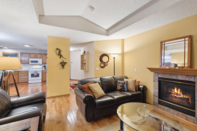 living room featuring light wood-type flooring, a fireplace, and a tray ceiling