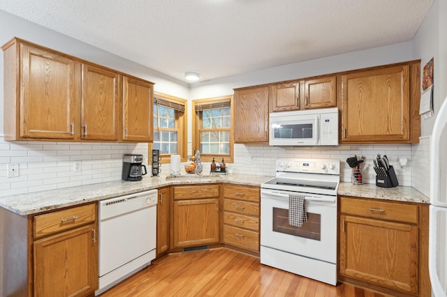 kitchen with white appliances, sink, tasteful backsplash, light hardwood / wood-style floors, and light stone counters