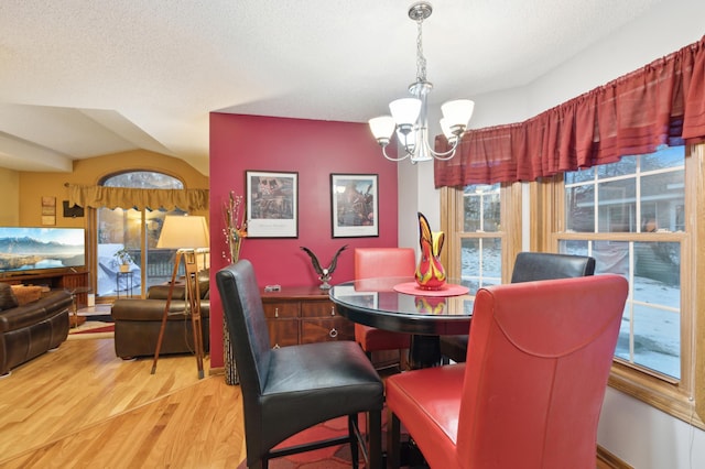 dining room featuring hardwood / wood-style flooring, a notable chandelier, a textured ceiling, and vaulted ceiling