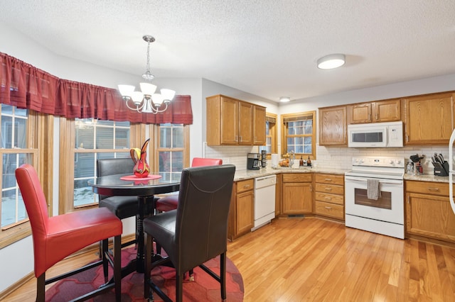 kitchen featuring light wood-type flooring, backsplash, white appliances, decorative light fixtures, and a notable chandelier