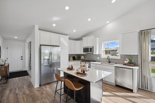 kitchen featuring a center island, sink, lofted ceiling, white cabinets, and appliances with stainless steel finishes