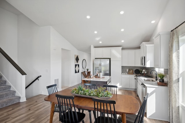 dining space featuring light wood-type flooring, lofted ceiling, and sink