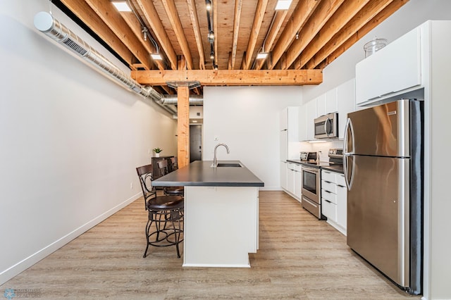 kitchen with a kitchen bar, sink, a center island with sink, stainless steel appliances, and white cabinets