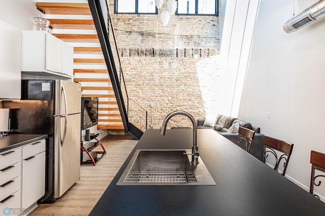 interior space featuring white cabinetry, sink, stainless steel refrigerator, and light wood-type flooring