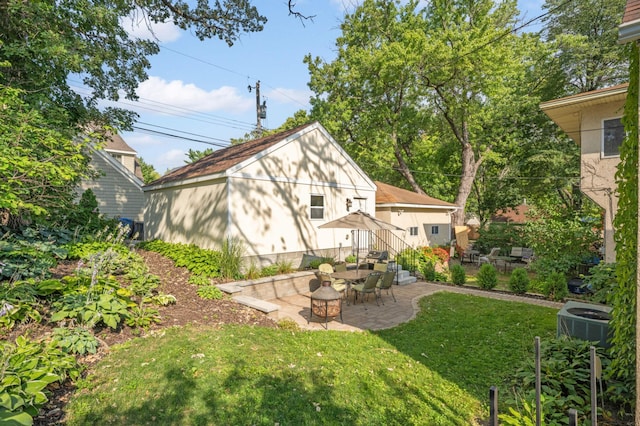 back of house featuring a lawn, an outbuilding, an outdoor fire pit, central AC, and a patio area