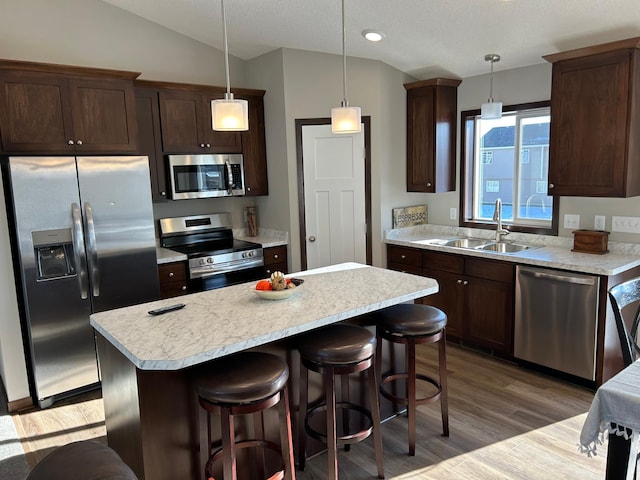 kitchen with sink, hanging light fixtures, appliances with stainless steel finishes, and a kitchen island