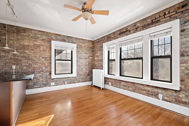 spare room featuring light wood-type flooring, radiator, ornamental molding, brick wall, and ceiling fan