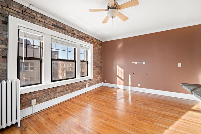 spare room with radiator, brick wall, ceiling fan, crown molding, and hardwood / wood-style flooring