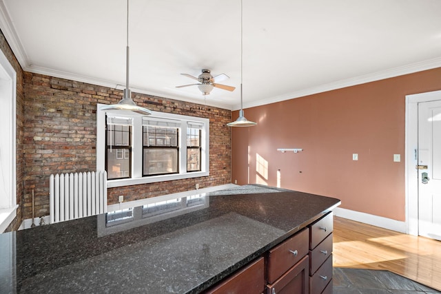 kitchen featuring pendant lighting, ceiling fan, dark stone countertops, and ornamental molding