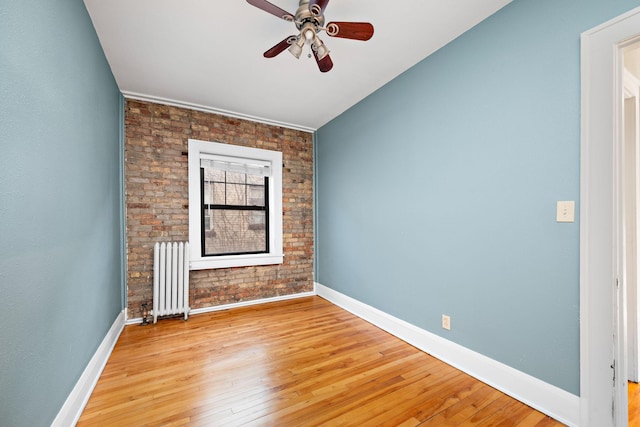 unfurnished room featuring radiator, ceiling fan, brick wall, light hardwood / wood-style floors, and lofted ceiling