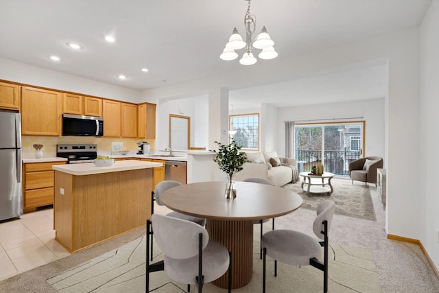 kitchen with stainless steel appliances, a chandelier, pendant lighting, light colored carpet, and a kitchen island