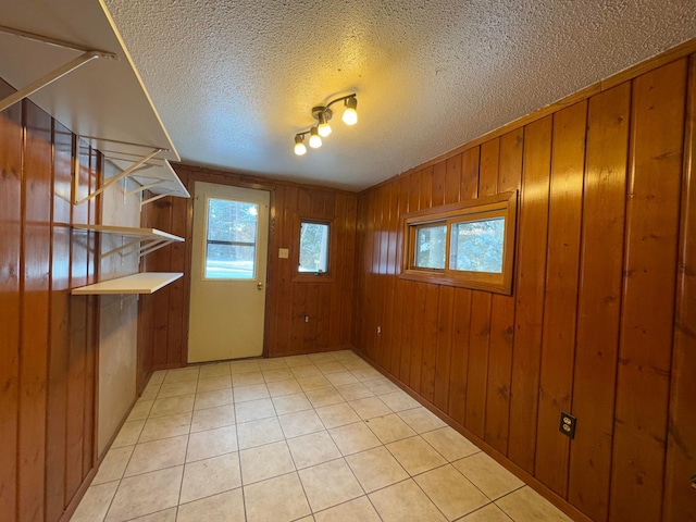 doorway to outside featuring wood walls, light tile patterned floors, a textured ceiling, and track lighting