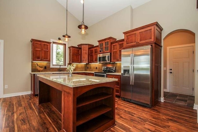 kitchen featuring hanging light fixtures, stainless steel appliances, light stone counters, backsplash, and an island with sink