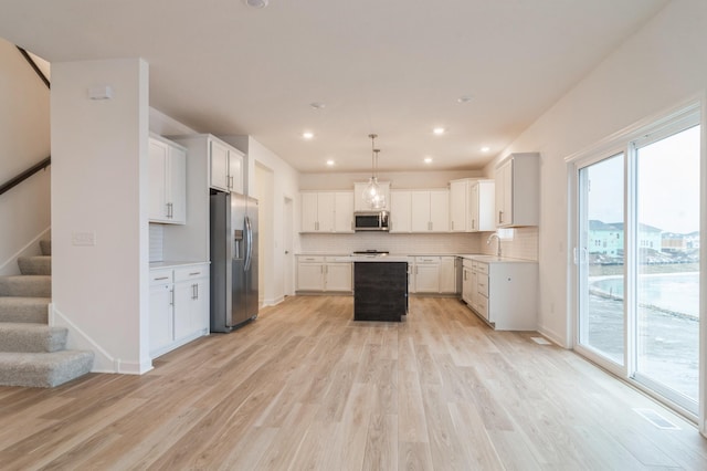 kitchen featuring pendant lighting, light wood-type flooring, appliances with stainless steel finishes, a kitchen island, and white cabinetry