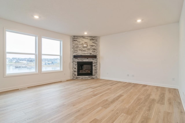 unfurnished living room featuring a stone fireplace and light hardwood / wood-style floors