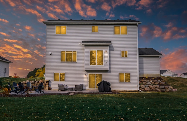 back house at dusk featuring a yard and a patio area