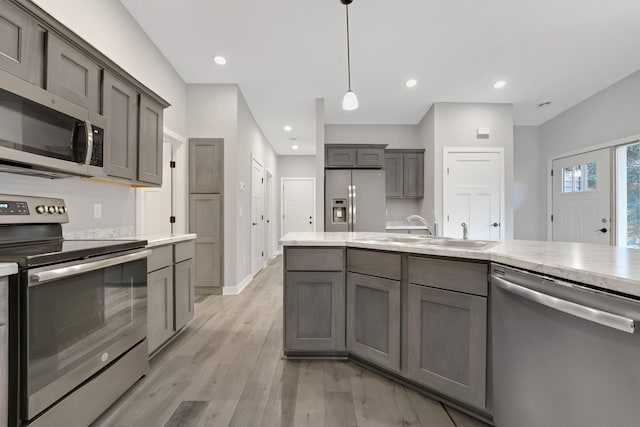 kitchen with sink, light wood-type flooring, stainless steel appliances, and hanging light fixtures