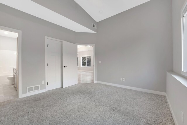 unfurnished bedroom featuring light carpet, connected bathroom, multiple windows, and lofted ceiling