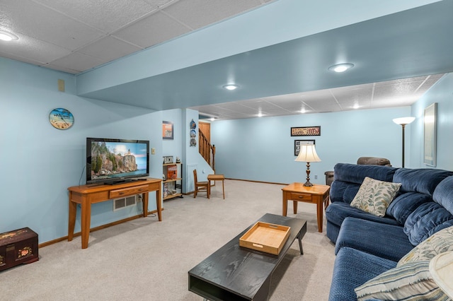 carpeted living area with stairs, a paneled ceiling, and baseboards