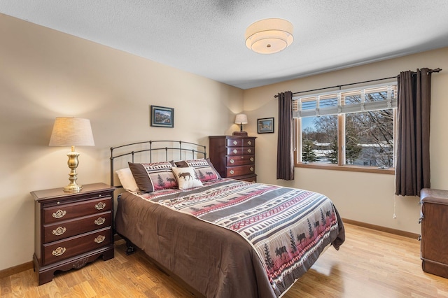 bedroom featuring light wood-style flooring, a textured ceiling, and baseboards