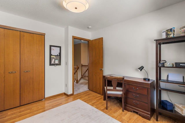 home office with light wood finished floors, a textured ceiling, and baseboards