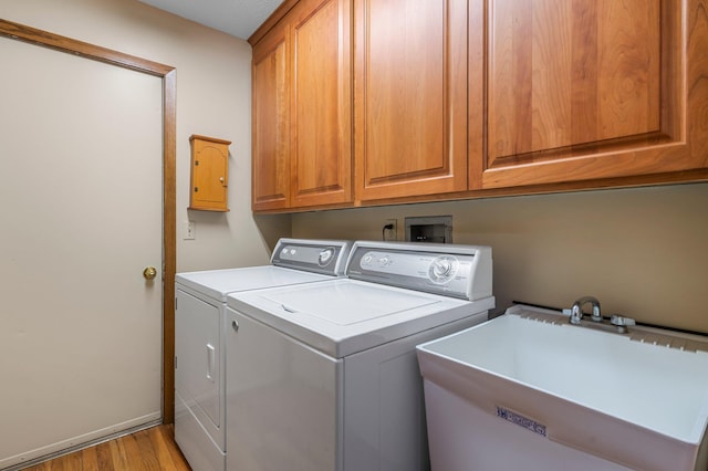 clothes washing area with baseboards, washing machine and dryer, light wood-type flooring, cabinet space, and a sink