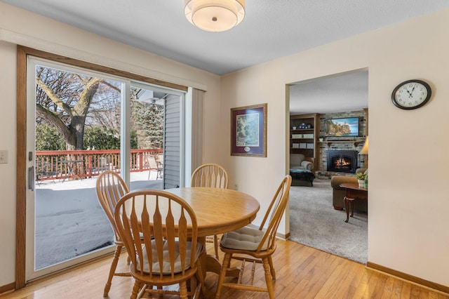 dining area with built in shelves, a textured ceiling, a large fireplace, light wood finished floors, and baseboards