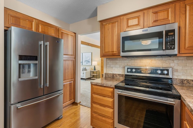 kitchen with decorative backsplash, light wood-style flooring, brown cabinetry, and appliances with stainless steel finishes