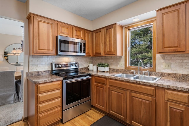 kitchen with brown cabinetry, a sink, light wood-style floors, appliances with stainless steel finishes, and tasteful backsplash