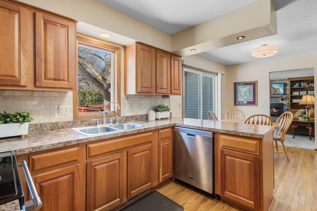 kitchen featuring light wood-style flooring, a sink, stainless steel dishwasher, a warm lit fireplace, and a peninsula