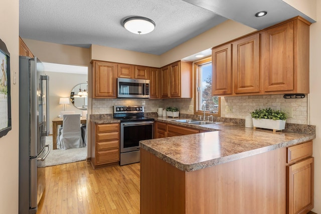 kitchen with light wood-type flooring, a peninsula, a sink, stainless steel appliances, and tasteful backsplash