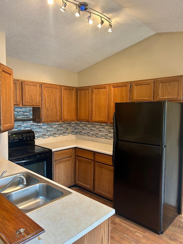 kitchen featuring sink, light hardwood / wood-style flooring, backsplash, lofted ceiling, and black appliances