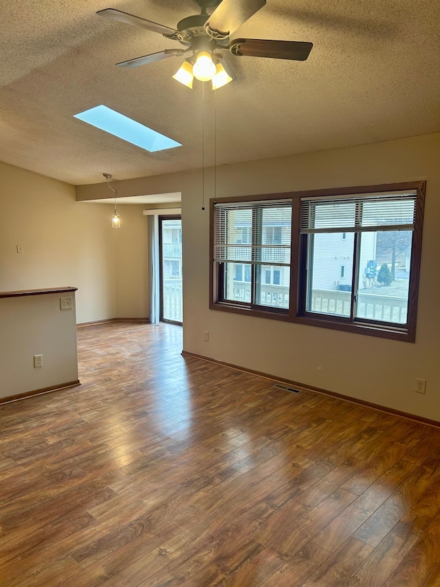 empty room with hardwood / wood-style floors, a textured ceiling, a skylight, and ceiling fan