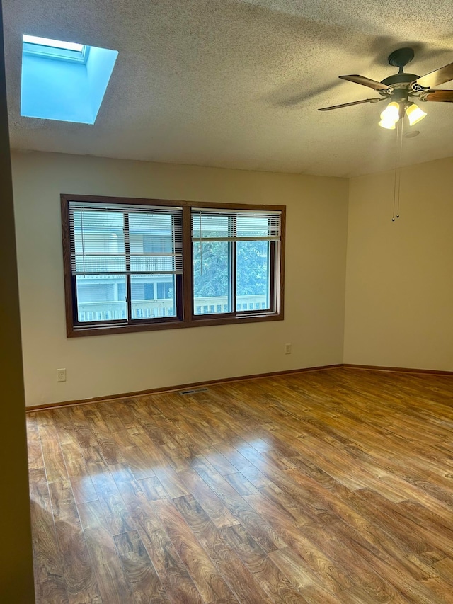 spare room with hardwood / wood-style floors, ceiling fan, a textured ceiling, and a skylight