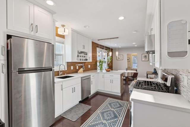 kitchen featuring pendant lighting, kitchen peninsula, sink, white cabinetry, and stainless steel appliances