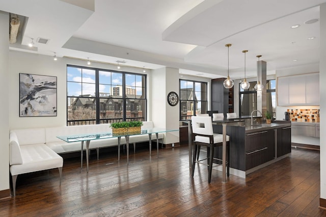 kitchen featuring dark wood-type flooring, a center island with sink, white cabinets, sink, and decorative light fixtures