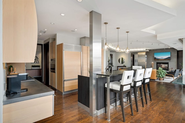 kitchen featuring stainless steel oven, dark wood-type flooring, built in refrigerator, pendant lighting, and a breakfast bar