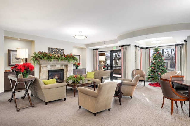 carpeted living room with a raised ceiling, plenty of natural light, and a high end fireplace