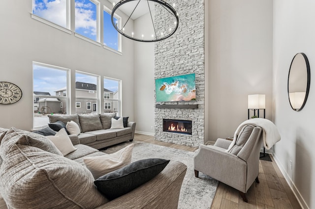 living room with a fireplace, a notable chandelier, wood-type flooring, and a high ceiling